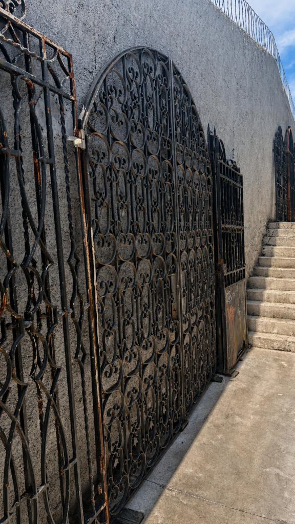 Portão antigo de ferro arqueado com desenhos ornamentais e detalhes artesanais.
